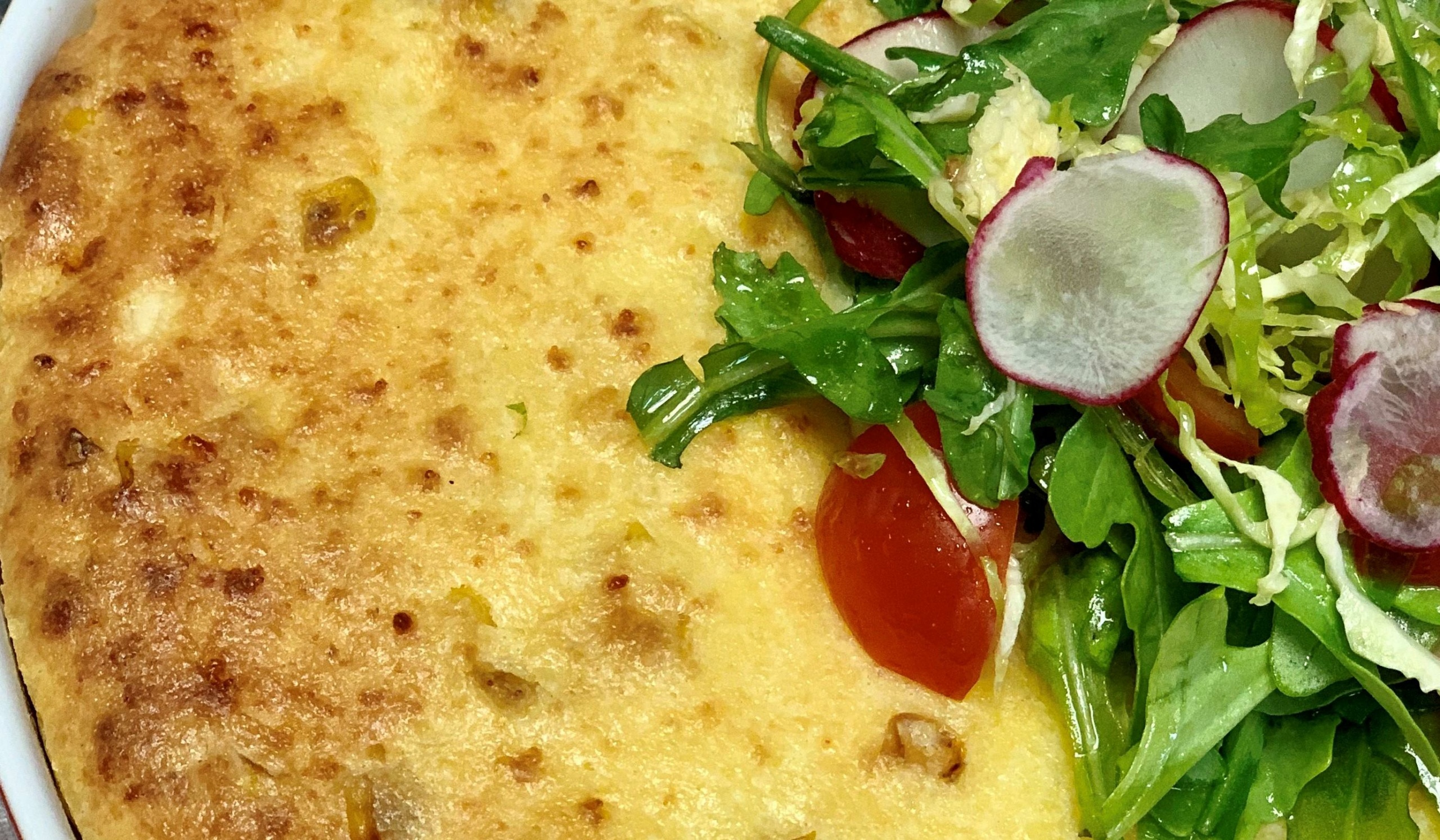 A close-up of a golden-brown omelette accompanied by a fresh salad. The salad features arugula, sliced radishes, shredded cabbage, and cherry tomatoes, adding vibrant green and red colors to the dish.