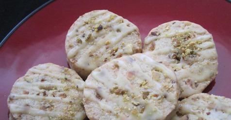 A red plate with several round, pistachio cookies, drizzled with a light glaze. The cookies display a light, crumbly texture with visible nut pieces.