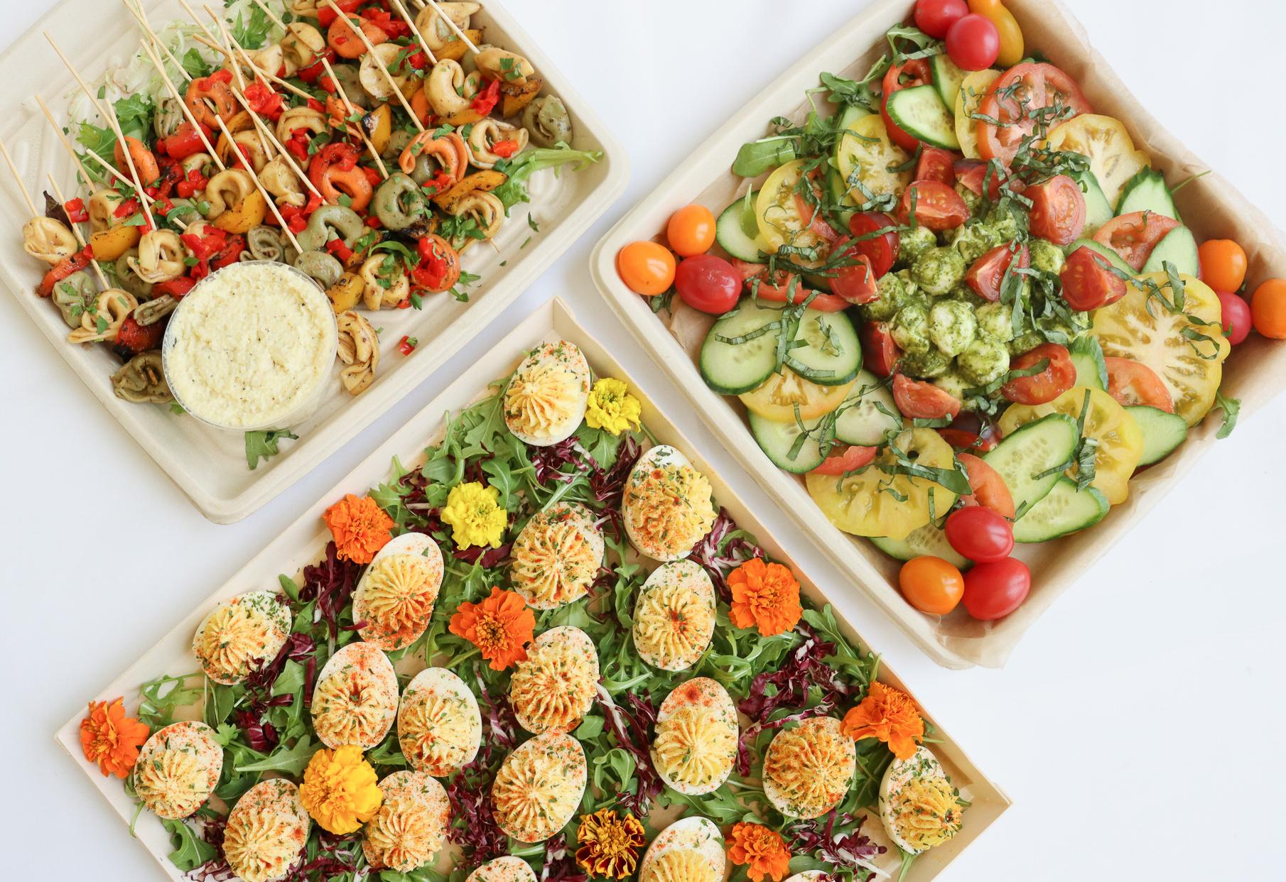 Three platters of colorful appetizers, including deviled eggs, skewers, and a cucumber-tomato salad.